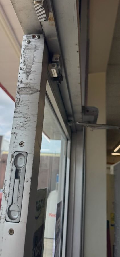 Damaged edge of a storefront entry door below the closer